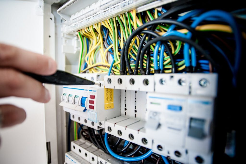 electrician-fixing-an-opened-switchboard-257736 Hand of electrician working on a circuit breaker panel with colorful wires, ensuring safe electrical connections.